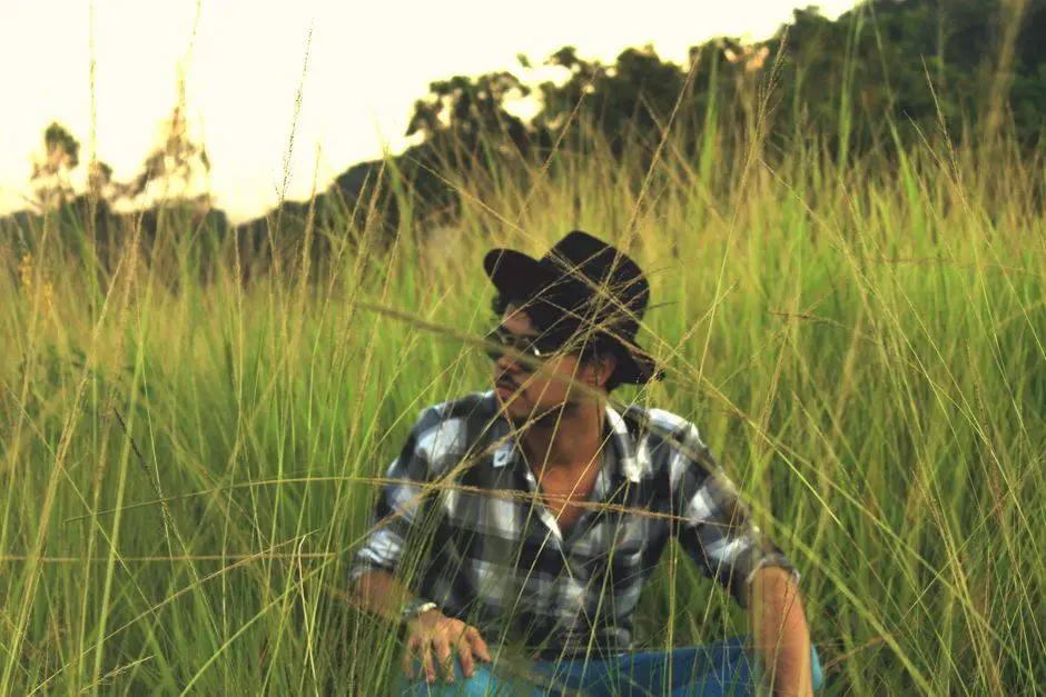 A man wearing sunglasses and a hat sits in a lush green field.