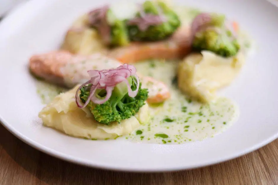 Close-up of a gourmet dish with salmon, broccoli, mashed potatoes, and garnishes.