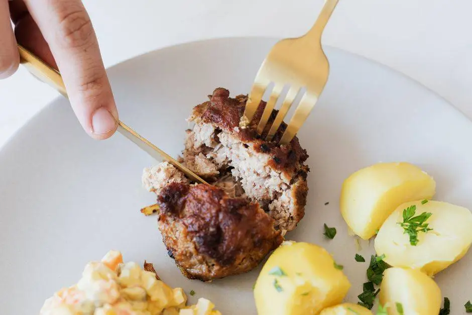 From above of crop faceless person with cutleries cutting tasty homemade fried meat cutlet garnished with boiled potatoes and parsley