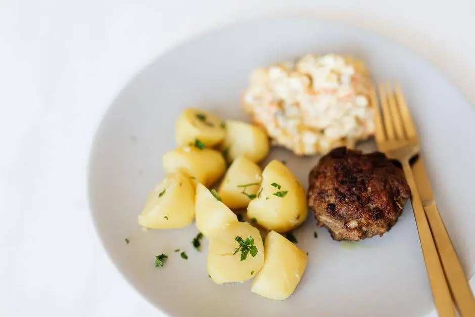 From above of homemade appetizing fried beef cutlet garnished with boiled potatoes with parsley and traditional Russian salad with meat potatoes green peas and mayo placed on plate with cutleries