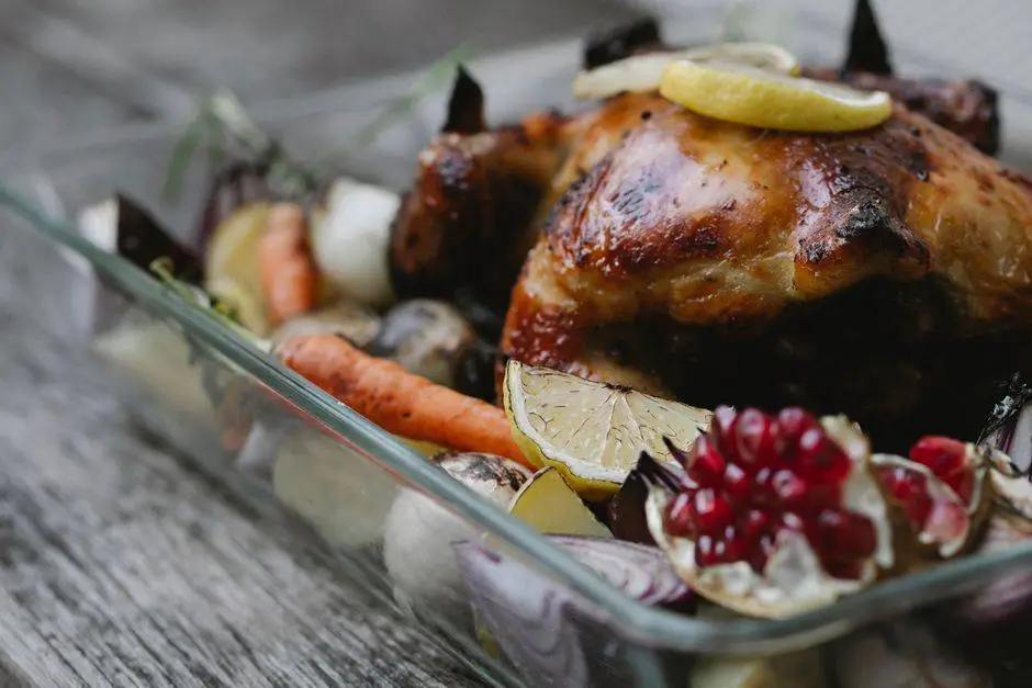 Delicious baked chicken with lemon slices and pomegranate seeds near whole carrots in glass baking pan on table